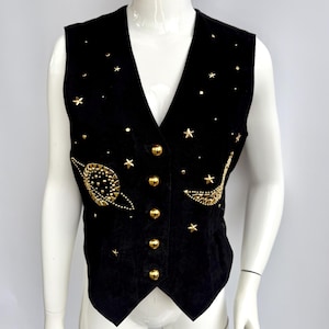 May include: Black suede vest with gold-colored star and planet embellishments. The vest has a V-neck, gold buttons, and a celestial design. The vest is sleeveless.