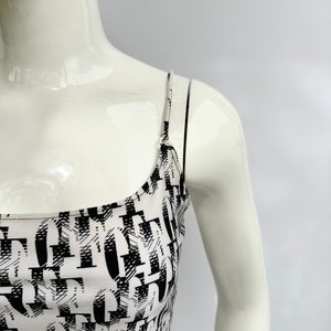 May include: A white tank top with black abstract print. The straps are thin and black.