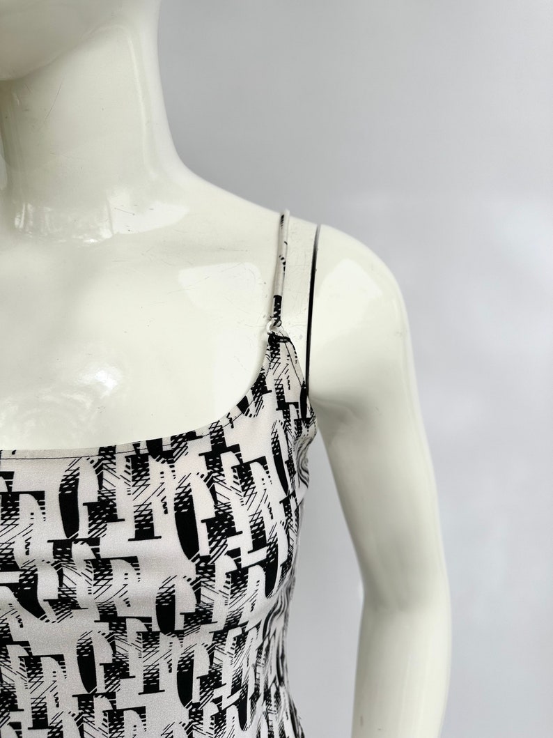 May include: A white tank top with black abstract print. The straps are thin and black.