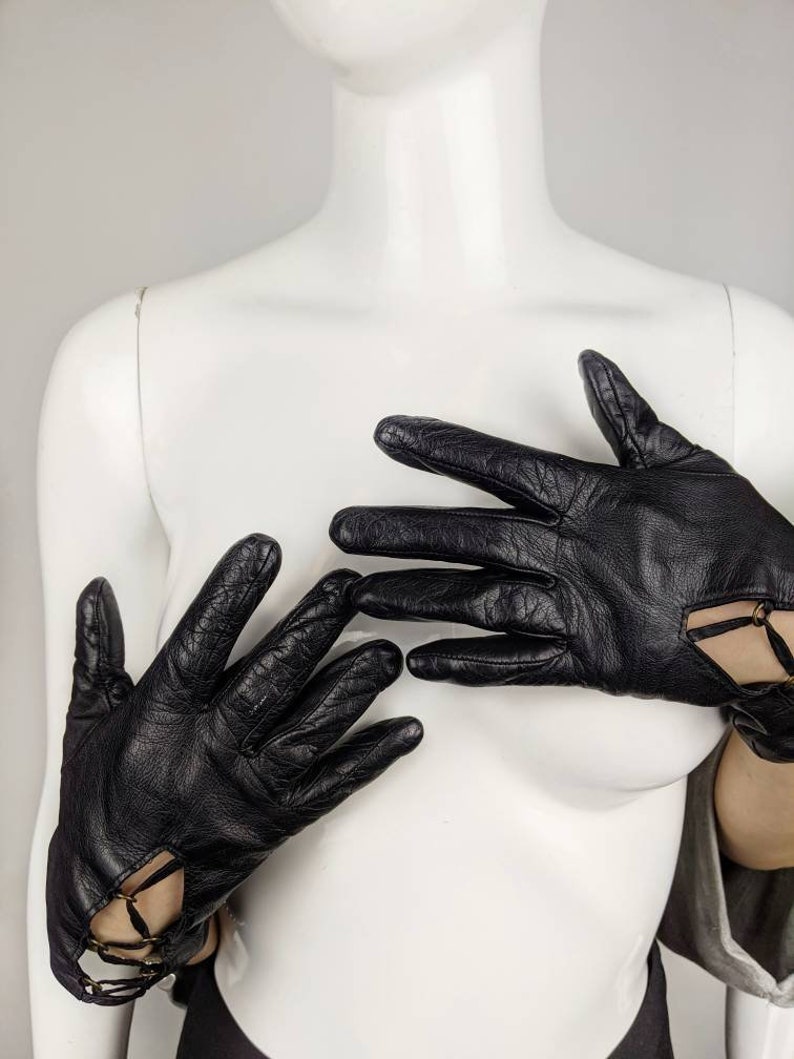 May include: A pair of black leather gloves with cut-out details and a chain accent.