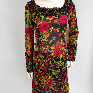 May include: A long-sleeved black dress with a vibrant floral pattern in red, green, orange, and blue. The dress features a ruffled neckline and cuffs. The text "SHRE MOSCHINO JEANS" is visible on the dress.