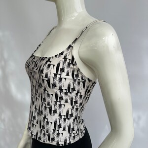 May include: A white tank top with a black and white abstract print. The tank top has thin straps and a scoop neck.