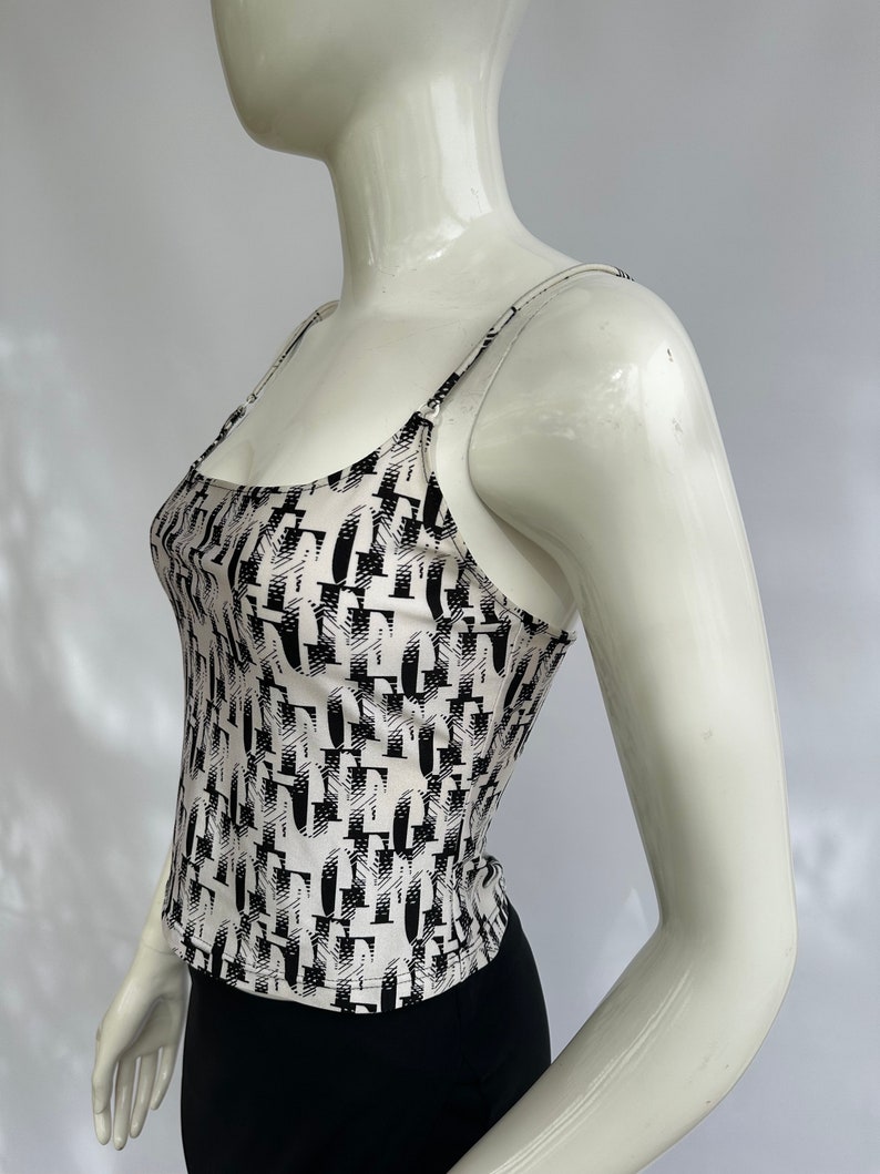 May include: A white tank top with a black and white abstract print. The tank top has thin straps and a scoop neck.