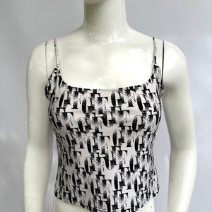 May include: A white tank top with a black and white abstract print. The print features a repeating pattern of geometric shapes and letters.
