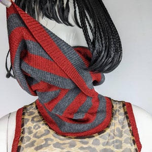 May include: A gray and red striped knit cowl neck scarf. The scarf is made of a soft, comfortable material and is perfect for layering in the fall and winter.