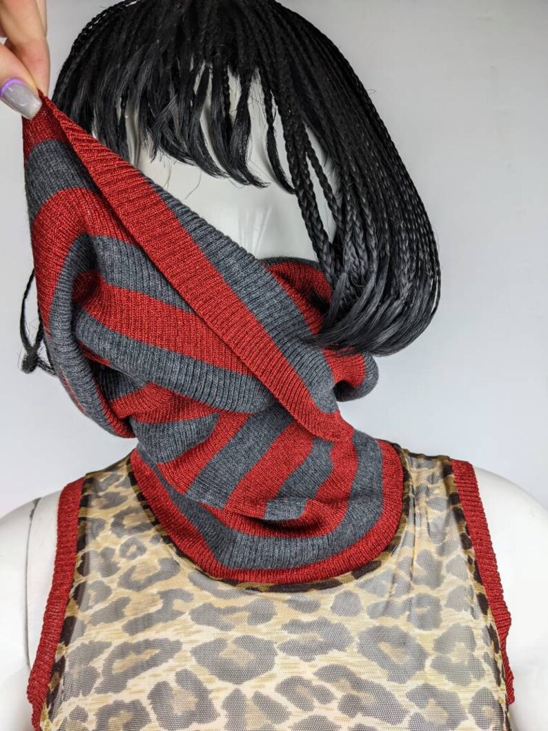 May include: A gray and red striped knit cowl neck scarf. The scarf is made of a soft, comfortable material and is perfect for layering in the fall and winter.