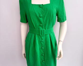 Puede incluir: Vestido verde brillante con cuello cuadrado y mangas cortas. El vestido tiene botones en la parte delantera y un cinturón a juego en la cintura. La tela tiene una apariencia texturizada. El vestido es de estilo rodilla.