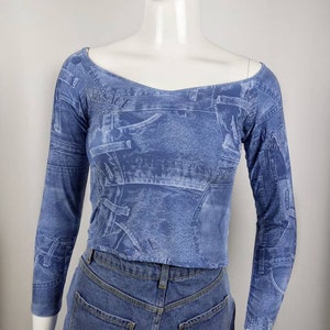 Pode incluir: Um top azul de manga comprida com estampa de jeans. O top tem um decote redondo e é feito de um tecido elástico.