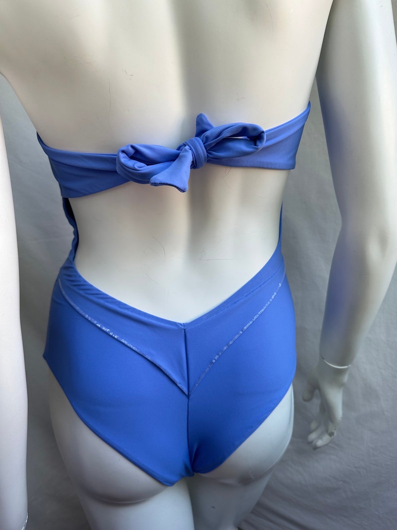 Pu&ograve; includere: Un costume da bagno intero blu pervinca con scollo all'americana e chiusura a fiocco sulla schiena. Il costume da bagno presenta un design a forma di V sul davanti e una schiena scoperta. Il tessuto &egrave; leggermente lucido.
