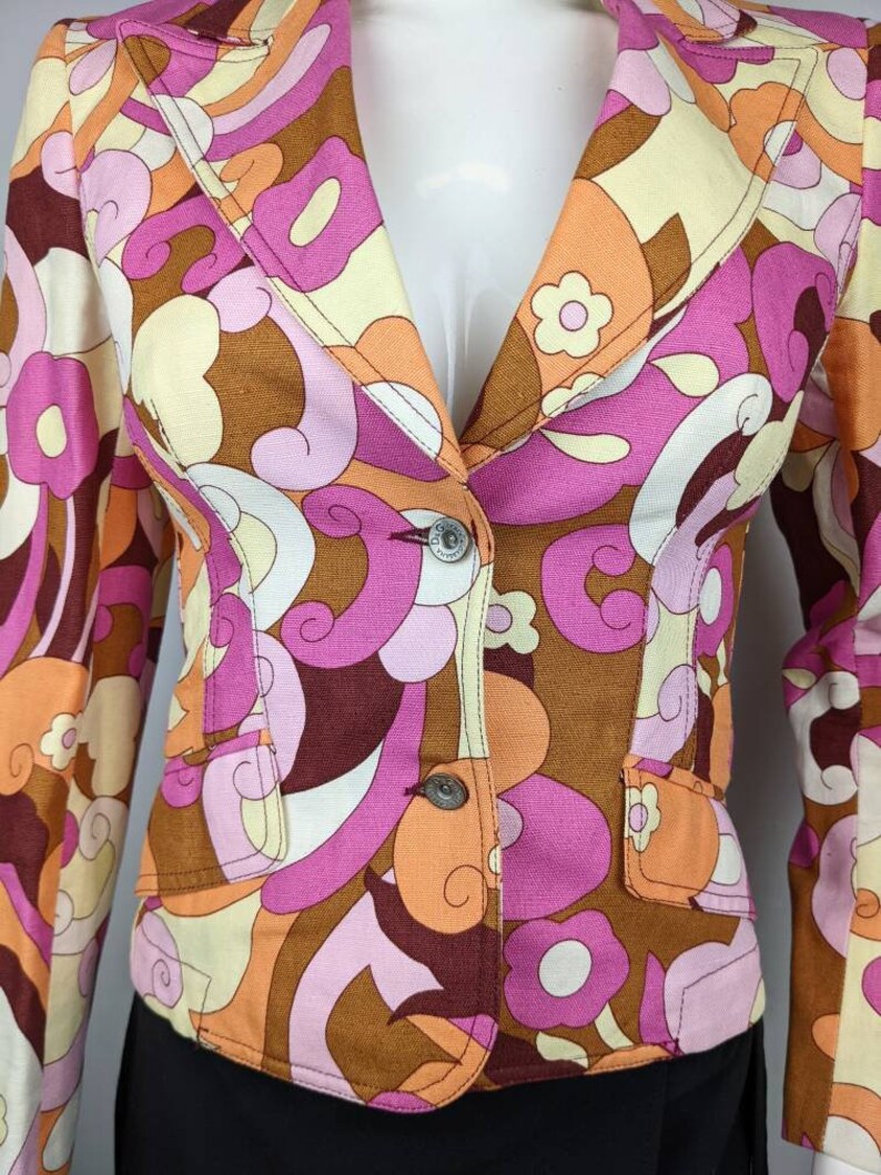 May include: A brown, pink, orange, and white patterned blazer with a button closure. The blazer has a retro 1970s style.