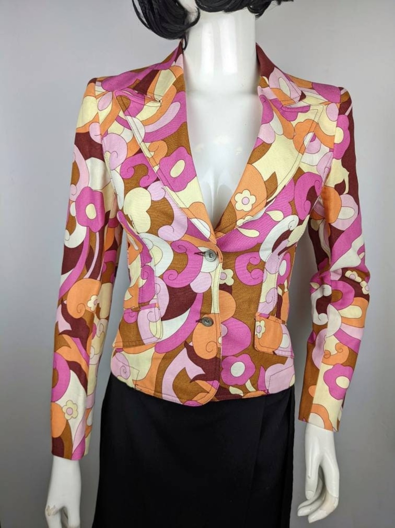 May include: A pink, orange, and brown patterned blazer with a single button closure. The blazer has a v-neck and long sleeves.