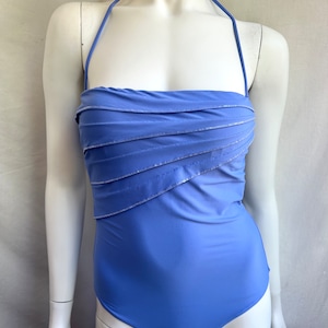 Pu&ograve; includere: Un costume da bagno blu pervinca con collo all'americana e corpetto arricciato. Il costume da bagno presenta accenti argentati lungo le linee arricciate, aggiungendo un tocco di brillantezza. Il design a un pezzo offre un look classico ed elegante.