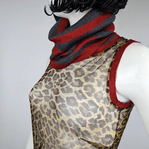 May include: A sheer sleeveless top with a leopard print pattern. The top has a red and gray striped turtleneck collar.