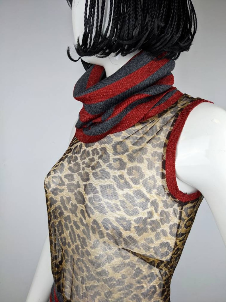 May include: A sheer sleeveless top with a leopard print pattern. The top has a red and gray striped turtleneck collar.