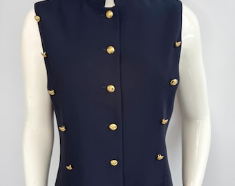 May include: A sleeveless navy blue dress with a mandarin collar and gold-colored buttons. The dress features decorative gold buttons on the shoulders and down the front, creating a classic and elegant look. The dress is displayed on a mannequin.