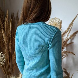 Puede incluir: Un su&eacute;ter azul claro de punto de canal&eacute; con mangas largas.