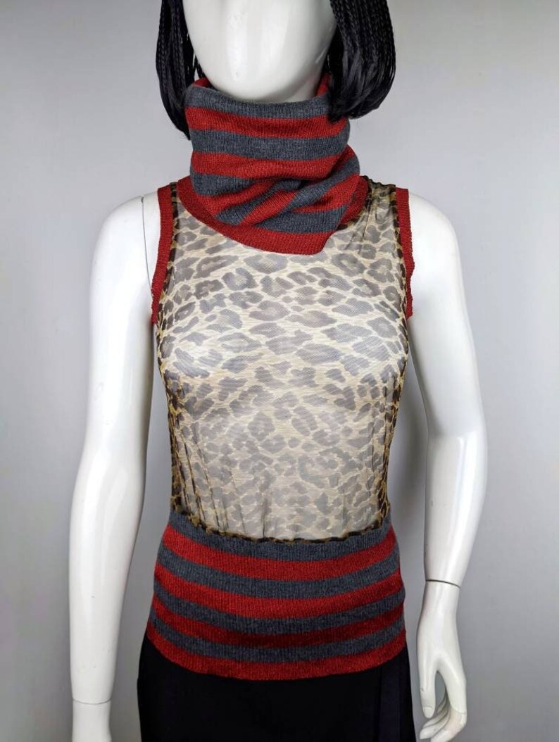 May include: A sheer sleeveless top with a leopard print pattern. The top has a red and gray striped turtleneck collar and a matching striped band at the bottom.