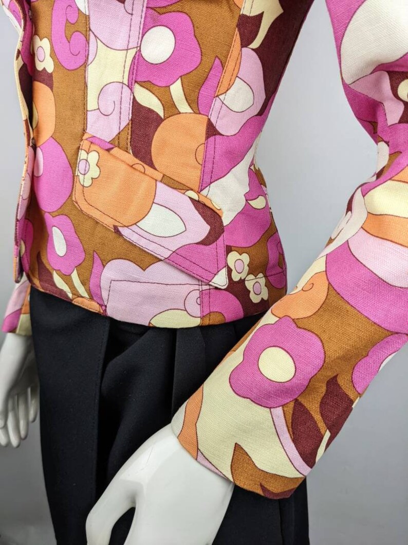 May include: A brown, pink, and cream patterned jacket with a fitted silhouette. The jacket has a button closure and long sleeves.
