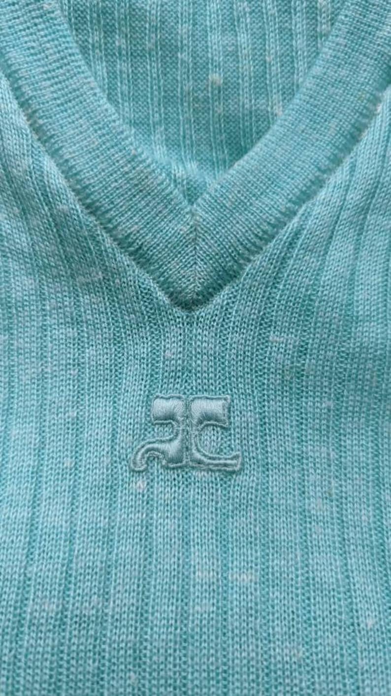 Puede incluir: Primer plano de una camisa de punto azul claro con un peque&ntilde;o logotipo bordado que dice "JC" en blanco.