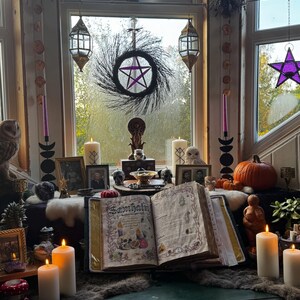 May include: A mystical display featuring a large open book with the word "Samhain" on the cover, surrounded by candles, a pentagram wreath, and various occult items. The scene is set near a window with hanging decorations.