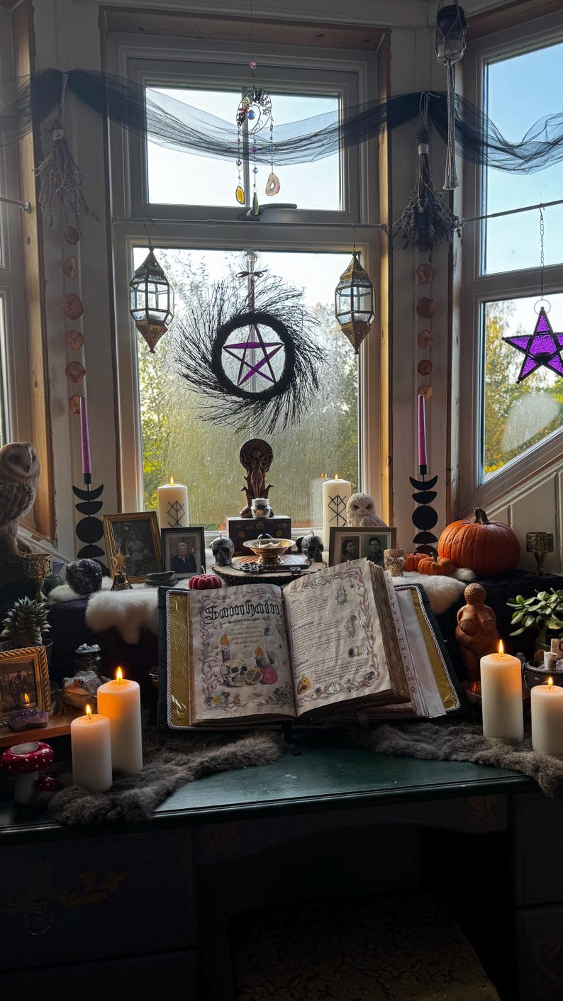 May include: A mystical display featuring a large open book with the word "Samhain" on the cover, surrounded by candles, a pentagram wreath, and various occult items. The scene is set near a window with hanging decorations.