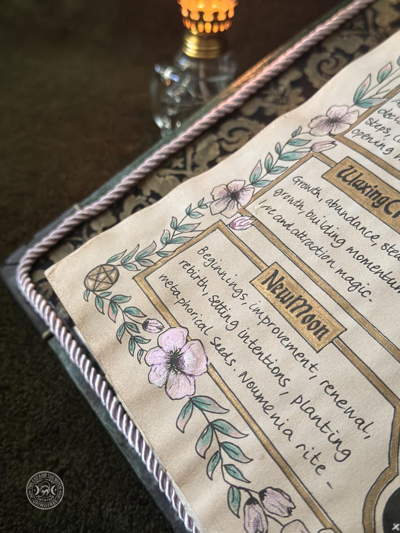 K&ouml;nnte beinhalten: Eine Seite aus einem Grimoire mit handgezeichneten Blumenr&auml;ndern und Text in Goldtinte. Der Text lautet New Moon, Beginnings, improvement, renewal, rebirth, setting intentions, planting metaphorical seeds, Noumenia rite, Waxing Crescent, Growth, abundance, steady growth, building momentum, love and attraction magic.