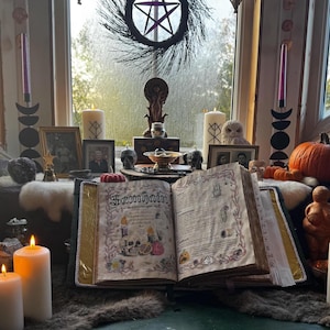 May include: An open book with the word "Samhain" on the cover, surrounded by candles, pumpkins, and decorative items. A wreath with a pentagram hangs in the background. The scene evokes a mystical or spiritual theme.