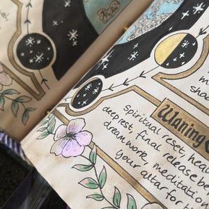 K&ouml;nnte beinhalten: Eine offene Buchseite mit handgezeichneten Illustrationen von Mondphasen, Sternen und Blumenranken. Der Text lautet Waning, spiritual reset, heal, deep rest, final release, be, dream work, meditation, your altar for the n.