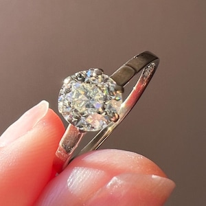 May include: A silver ring with a large, round, clear diamond set in a halo setting.
