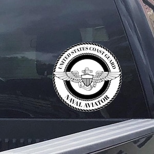 May include: A circular black and white sticker featuring the United States Coast Guard Naval Aviator emblem. The emblem includes wings, an anchor, and the text "United States Coast Guard" and "Naval Aviator" in a circular design.