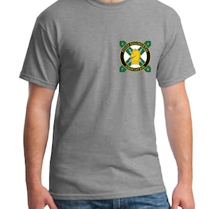 May include: A gray t-shirt featuring a small emblem on the left chest. The emblem is a circular design with a yellow horse figure at the center, surrounded by green and black details and the text "PSYOP REGIMENTAL ASSOCIATION".
