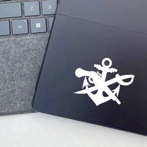 May include: White vinyl sticker of a nautical anchor, sword, and pistol design on a black laptop.