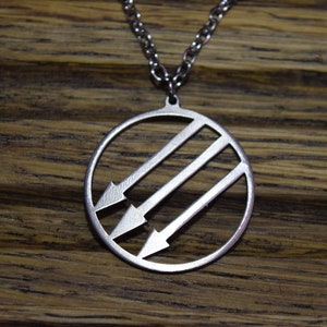 May include: A silver necklace with a circular pendant featuring three arrows pointing to the left inside a circle. The pendant is made of metal and has a shiny finish.