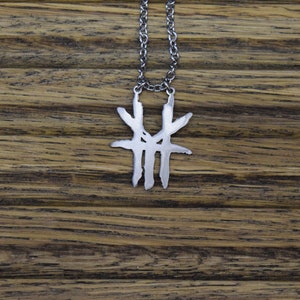 May include: A silver necklace with a pendant shaped like a stylized abstract design. The pendant is made of metal and has a rough, textured surface.