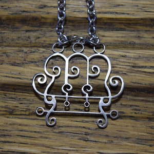 以下が含まれることがあります： 渦巻き模様が施された、3つの輪が絡み合ったスタイリッシュなデザインのシルバーペンダントがついたシルバーネックレス。ペンダントはシルバーチェーンに繋がっています。