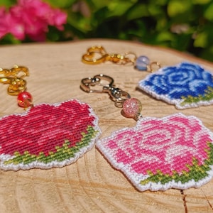 Peut inclure: Trois porte-clés en forme de rose brodée avec des motifs floraux rouges, roses et bleus et des accents de feuilles vertes. Chaque porte-clés comprend un fermoir mousqueton en métal et une perle décorative rouge, rose ou bleue.