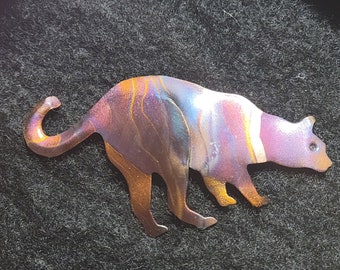 May include: A metal cat sculpture with a purple, blue, and orange iridescent finish. The cat is in a crouching position with its tail curled around its body.