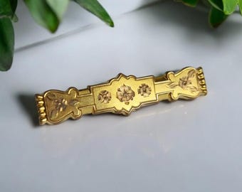 May include: A gold-toned brooch with a floral design. The brooch is made of metal and has a detailed, intricate pattern.