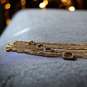 May include: A gold chain necklace with multiple strands and oval-shaped brown gemstones.
