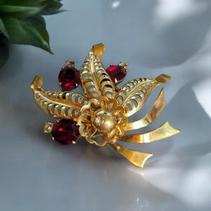 May include: A gold-toned brooch with a floral design and red and clear rhinestones.