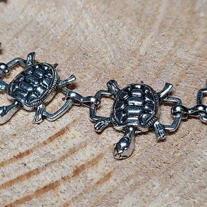 May include: Silver chain bracelet with turtle charms. Each turtle charm has a detailed shell design.