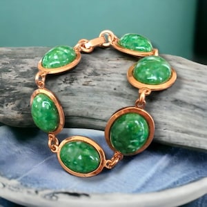 May include: A copper bracelet with six oval-shaped green stones. The stones have a marbled pattern.
