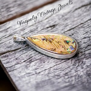 May include: A teardrop-shaped pendant with a silver setting and a colorful iridescent abalone shell inlay. The pendant is resting on a weathered wooden surface. The text "Vaguely Vintage Jewels" is visible in the background.