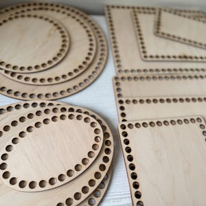 Op de afbeelding: Een verzameling onafgewerkte houten mandbodems in verschillende vormen en maten. De bodems omvatten ronde, ovale en vierkante vormen, elk met gelijkmatig verdeelde gaten voor het weven. Het hout heeft een lichte, natuurlijke kleur.