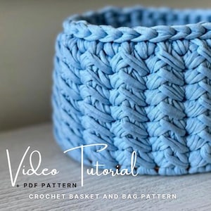 以下が含まれることがあります： テクスチャードデザインのライトブルーのかぎ針編みバスケット。バスケットは編み込みのトップエッジがあり、柔らかい織り素材で作られています。画像には「Video Tutorial + PDF Pattern Crochet Basket and Bag Pattern English and Bulgarian」と書かれています。