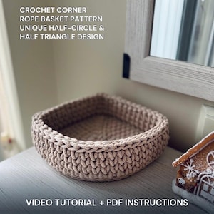 Puede incluir: Una cesta de esquina de ganchillo beige con un diseño único de medio círculo y medio triángulo. La cesta está hecha a mano y se encuentra sobre una superficie de color claro. El texto de la imagen dice: "CROCHET CORNER ROPE BASKET PATTERN UNIQUE HALF-CIRCLE & HALF TRIANGLE DESIGN VIDEO TUTORIAL + PDF INSTRUCTIONS."