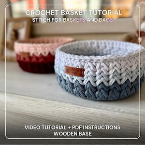May include: Two handmade crochet baskets. One is white, gray, and blue, with a leather tag. The other is pink and burgundy. The image includes text that reads "CROCHET BASKET TUTORIAL STITCH FOR BASKETS AND BAGS VIDEO TUTORIAL + PDF INSTRUCTIONS WOODEN BASE."