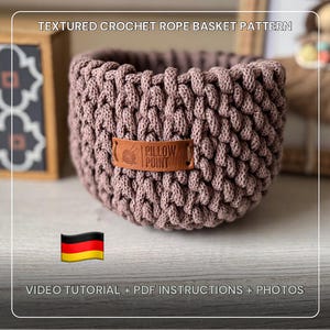 May include: A mauve crochet rope basket with a textured design and a leather label reading "Pillow Point". The basket is cylindrical and has a woven pattern. The text "TEXTURED CROCHET ROPE BASKET PATTERN" is visible at the top.