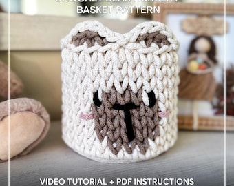 May include: A crocheted bear-shaped nursery basket in cream, brown, and black. The basket features a bear face design with a brown snout, black eyes, and pink cheeks. The text "CROCHET BEAR NURSERY BASKET PATTERN" and "VIDEO TUTORIAL + PDF INSTRUCTIONS" are visible.