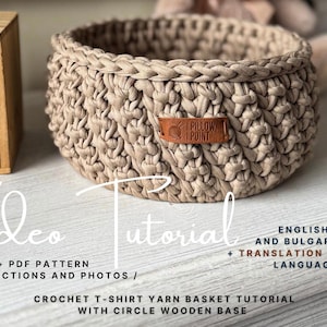 May include: A beige crocheted basket with a leather tag that reads "PILLOW POINT". The basket is round with a braided rim. Text on the image says "Video Tutorial" and "Crochet T-shirt Yarn Basket Tutorial".